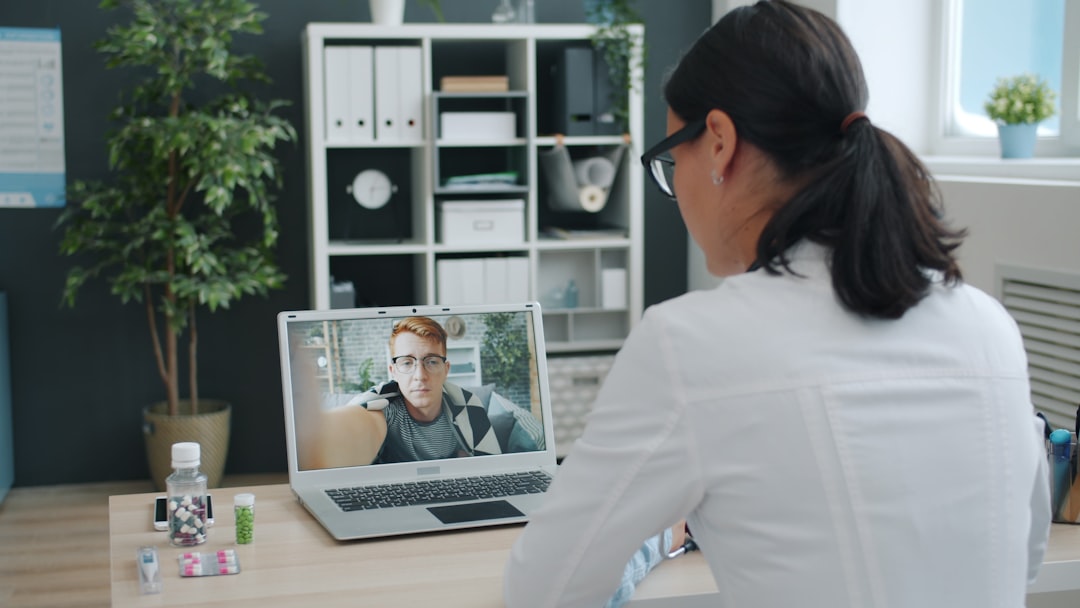 Medic young woman in uniform is talking to sick man online using computer from clinic office discussing pills and prescribing treatment in internet.