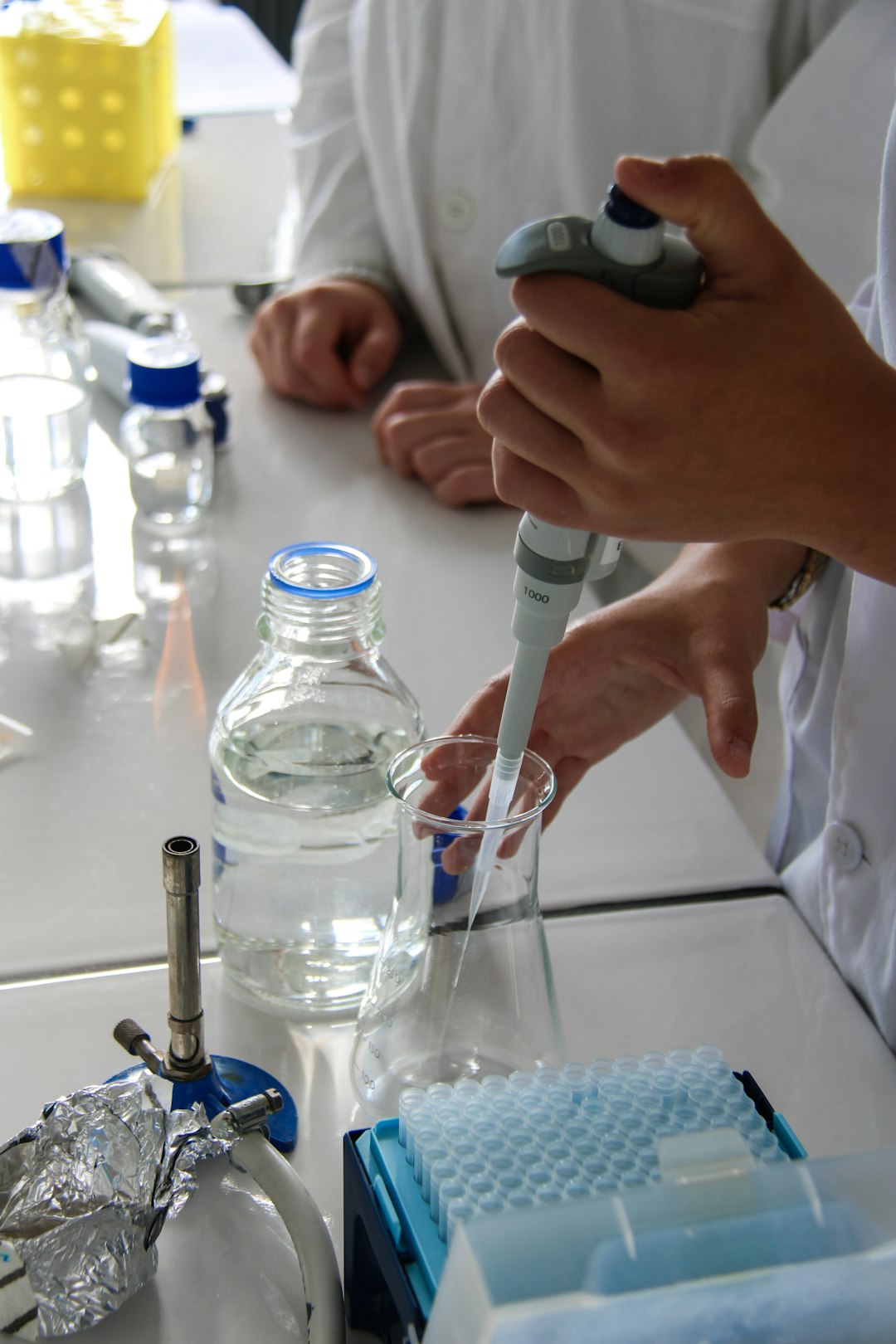 A technician pouring liquid into an erlenmeyer with a micropipette in a science laboratory. The experience is done in semi-sterile condition close to a flame.